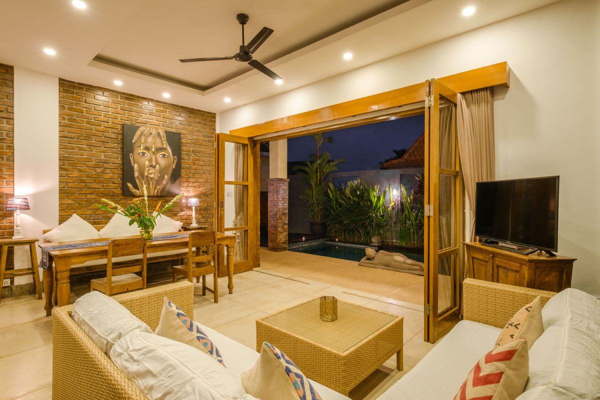 Rustic Balinese villa kitchen and dining room with wooden cabinets, stone walls, and views of traditional temple roofs. - Bali Villas