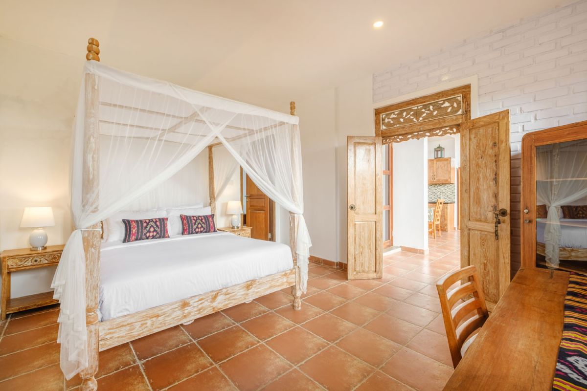 Rustic Balinese villa kitchen and dining room with wooden cabinets, stone walls, and views of traditional temple roofs. - Bali Villas