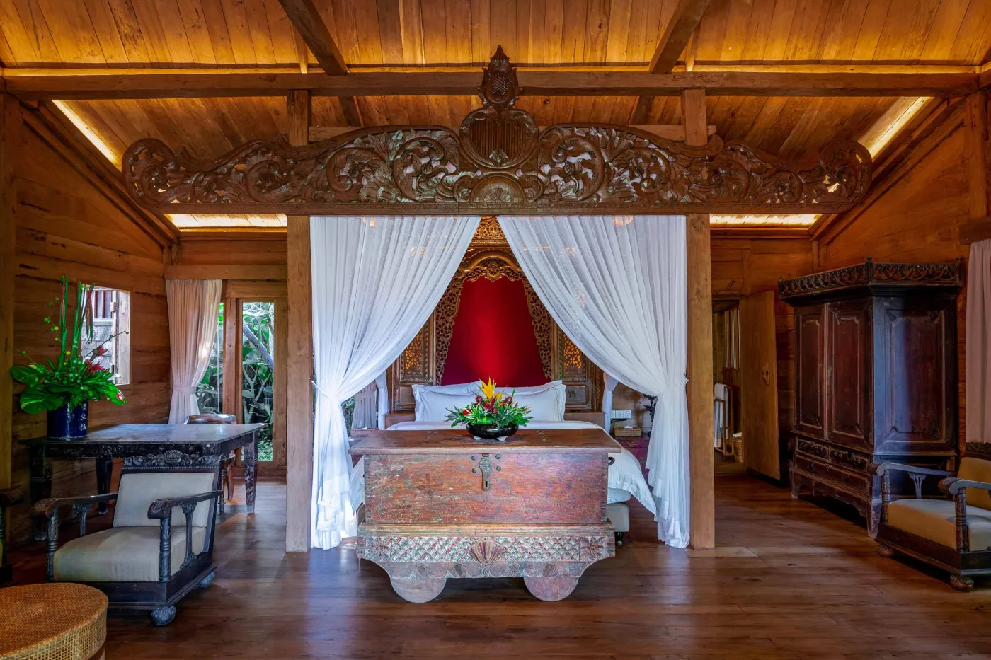 Open-air tropical resort bar with carved wooden counter, thatched roof, backlit liquor shelves, fresh fruits, and surrounding lush greenery. - Bali Villas