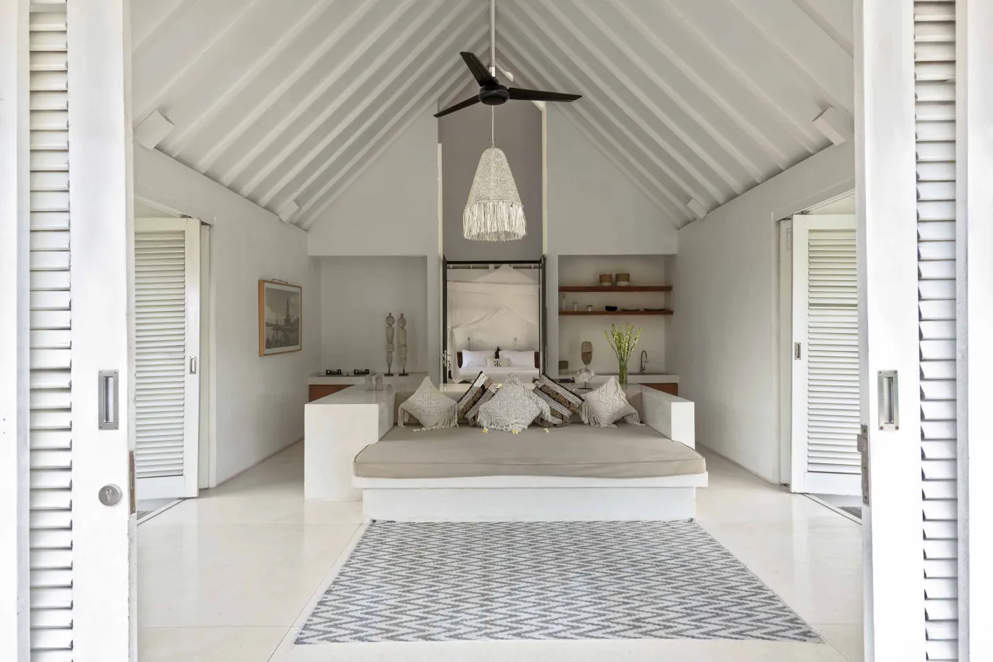 Spacious open-air Balinese villa lounge with white columns, tropical greenery, hanging hammocks, and carved wooden furniture. - Bali Villas