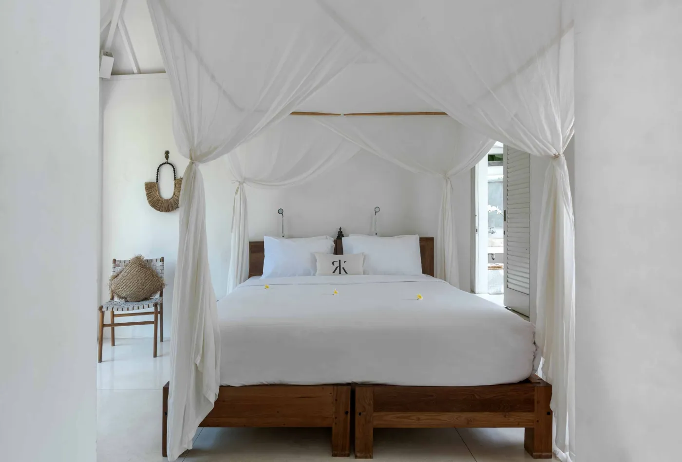 Spacious open-air Balinese villa lounge with white columns, tropical greenery, hanging hammocks, and carved wooden furniture. - Bali Villas