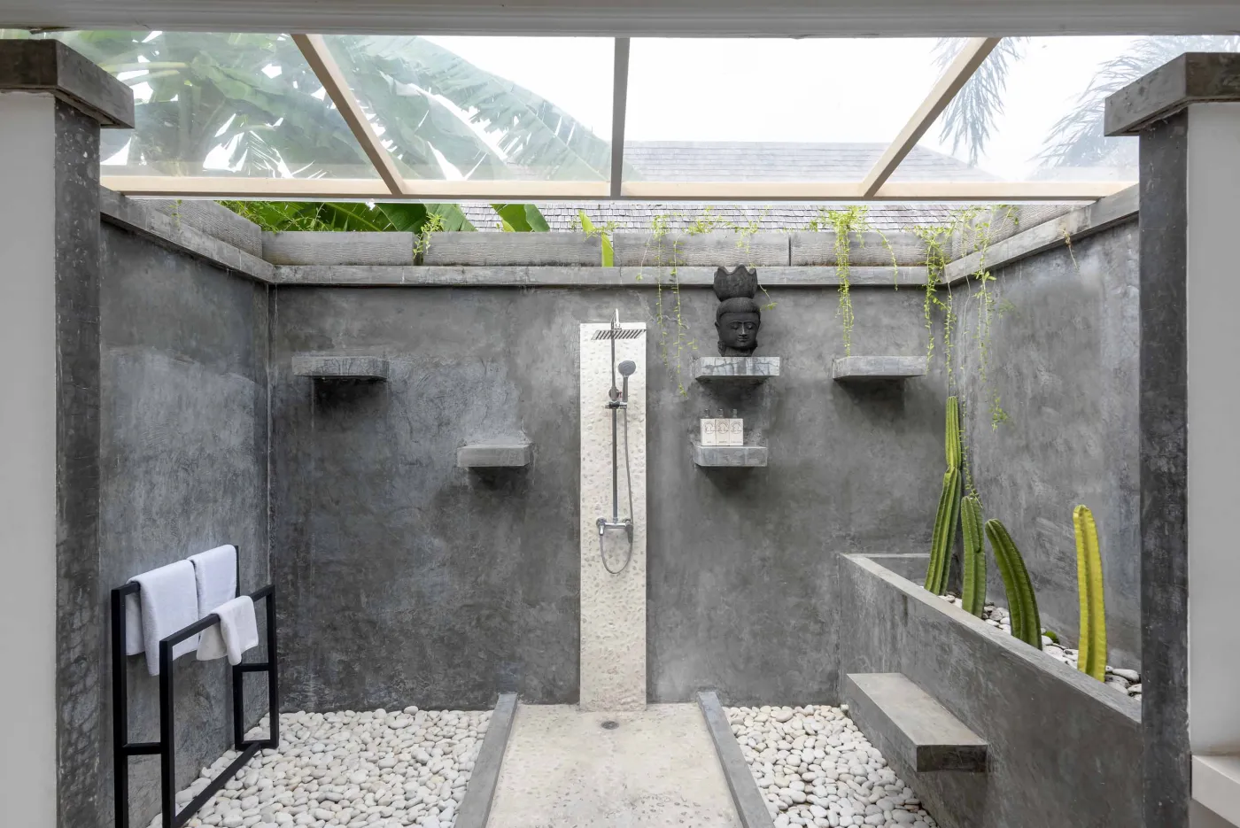 Spacious open-air Balinese villa lounge with white columns, tropical greenery, hanging hammocks, and carved wooden furniture. - Bali Villas