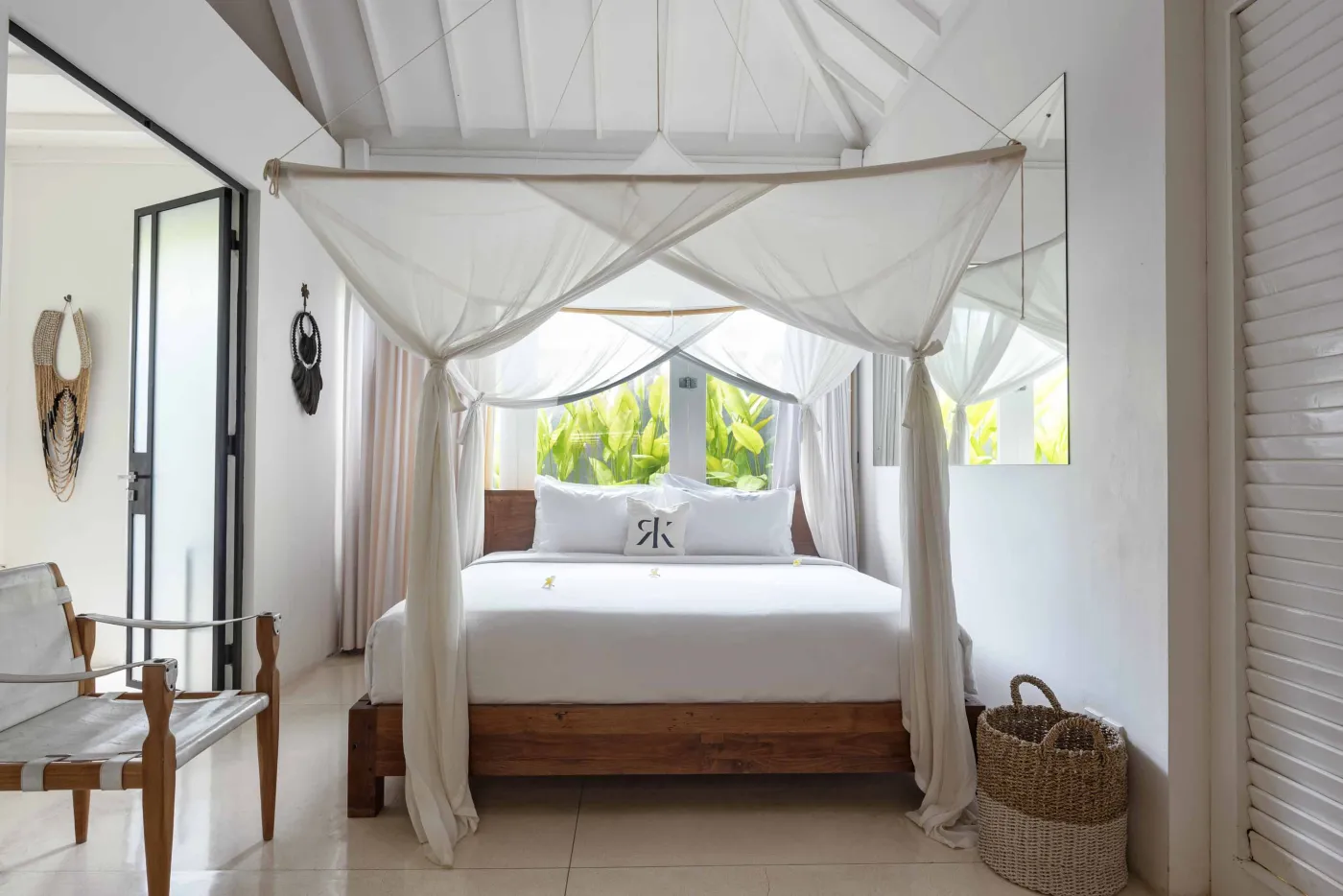 Spacious open-air Balinese villa lounge with white columns, tropical greenery, hanging hammocks, and carved wooden furniture. - Bali Villas