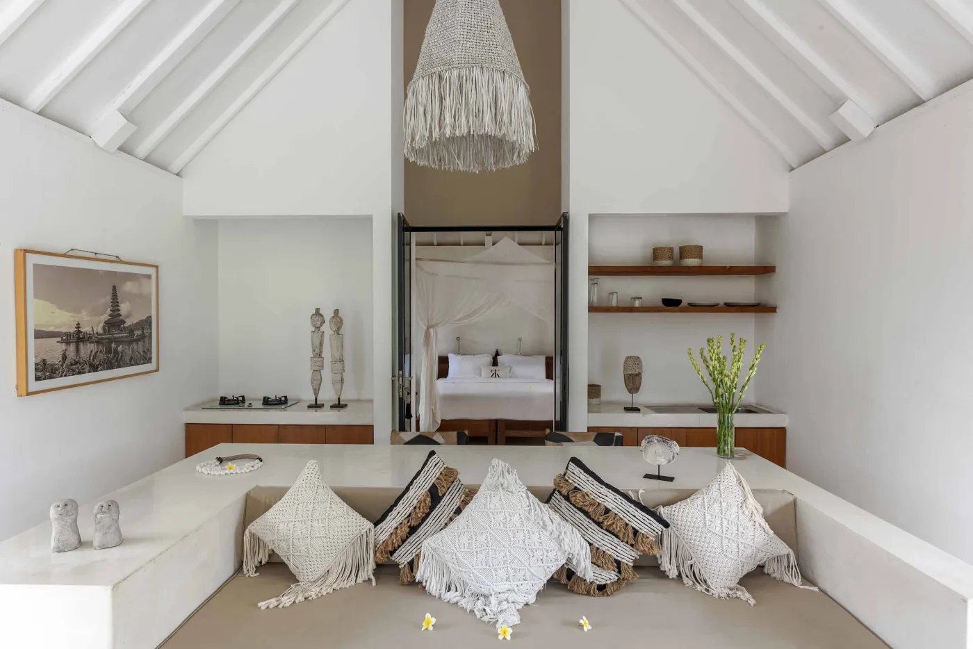 Spacious open-air Balinese villa lounge with white columns, tropical greenery, hanging hammocks, and carved wooden furniture. - Bali Villas