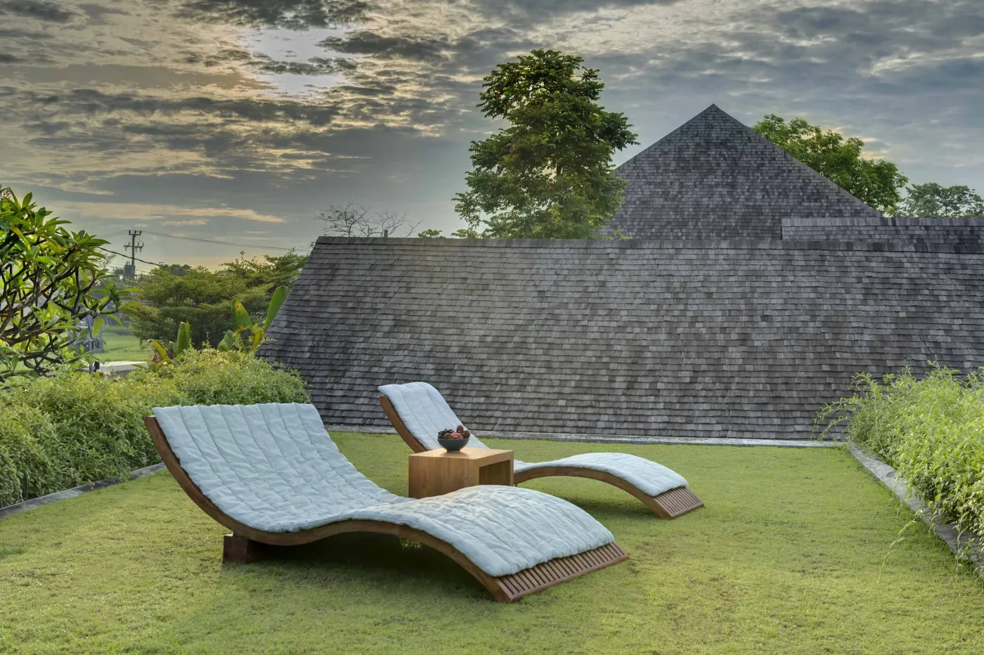 Serene tropical outdoor deck in a Bali villa featuring a stone bathtub filled with rose petals, lounge chairs, towels, and lush greenery. - Bali Villas