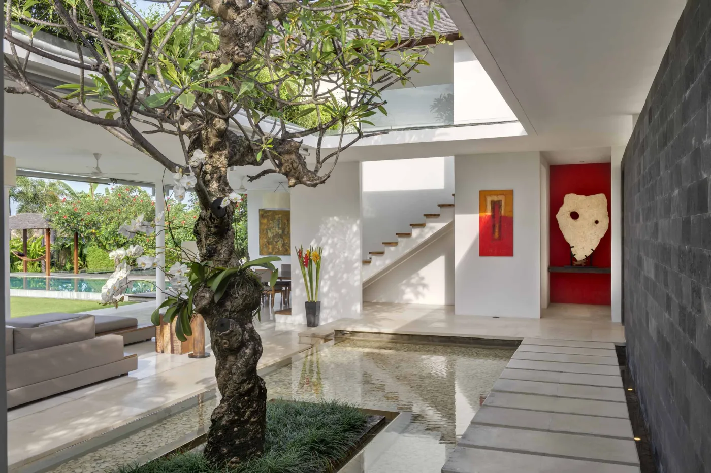 Serene tropical outdoor deck in a Bali villa featuring a stone bathtub filled with rose petals, lounge chairs, towels, and lush greenery. - Bali Villas