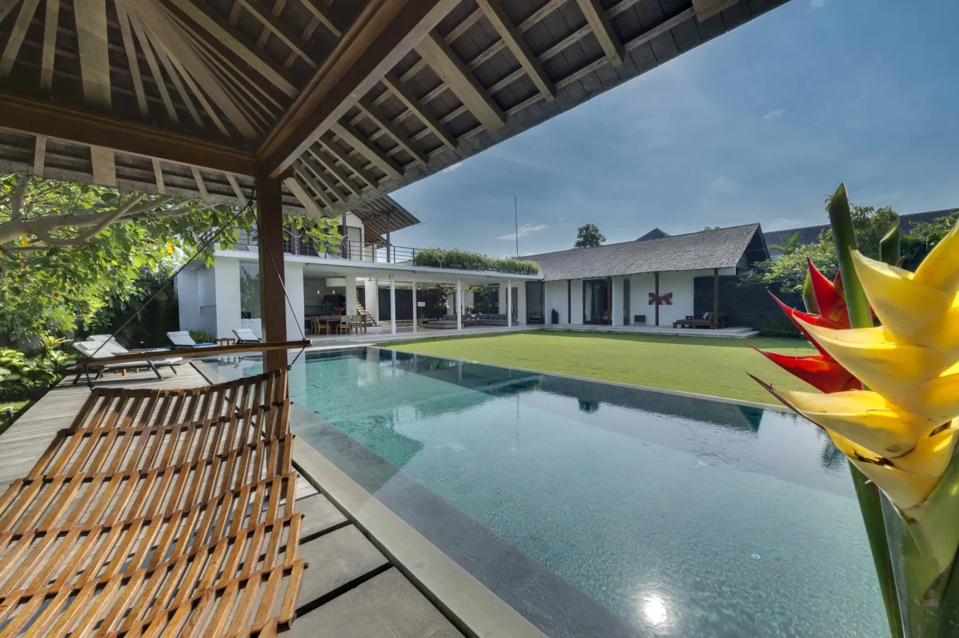 Serene tropical outdoor deck in a Bali villa featuring a stone bathtub filled with rose petals, lounge chairs, towels, and lush greenery. - Bali Villas