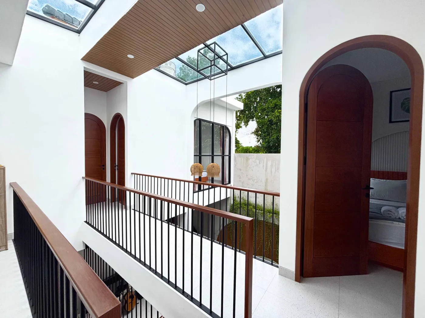 Modern tropical villa kitchen and dining area with orange cabinets, wooden ceiling, pendant lights, and outdoor pool view featuring a statue. - Bali Villas
