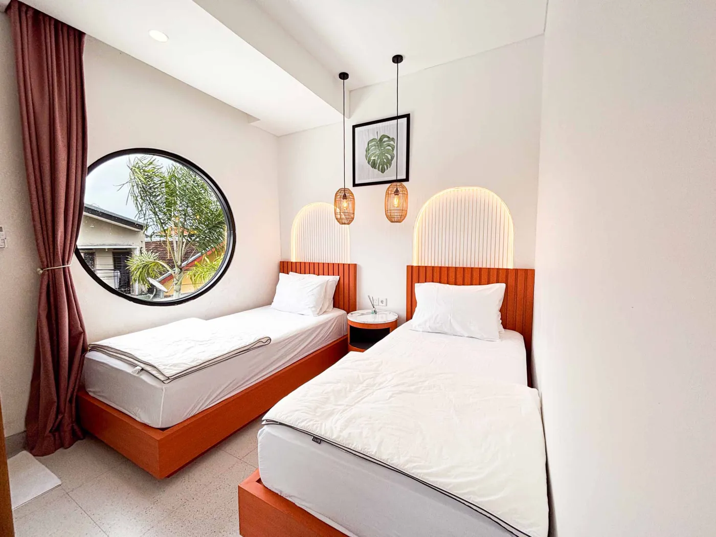 Modern tropical villa kitchen and dining area with orange cabinets, wooden ceiling, pendant lights, and outdoor pool view featuring a statue. - Bali Villas