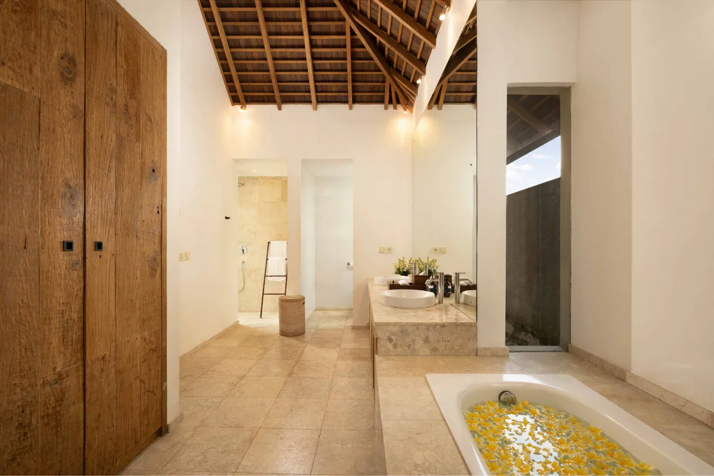 Spacious open-plan living and dining area in a modern tropical villa with exposed wooden beams, white walls, hardwood floors, and large windows. - Bali Villas