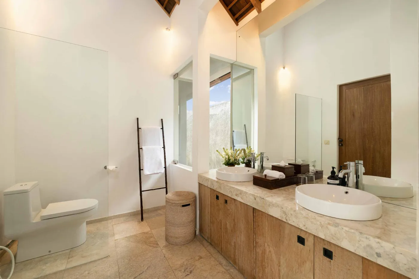 Spacious open-plan living and dining area in a modern tropical villa with exposed wooden beams, white walls, hardwood floors, and large windows. - Bali Villas