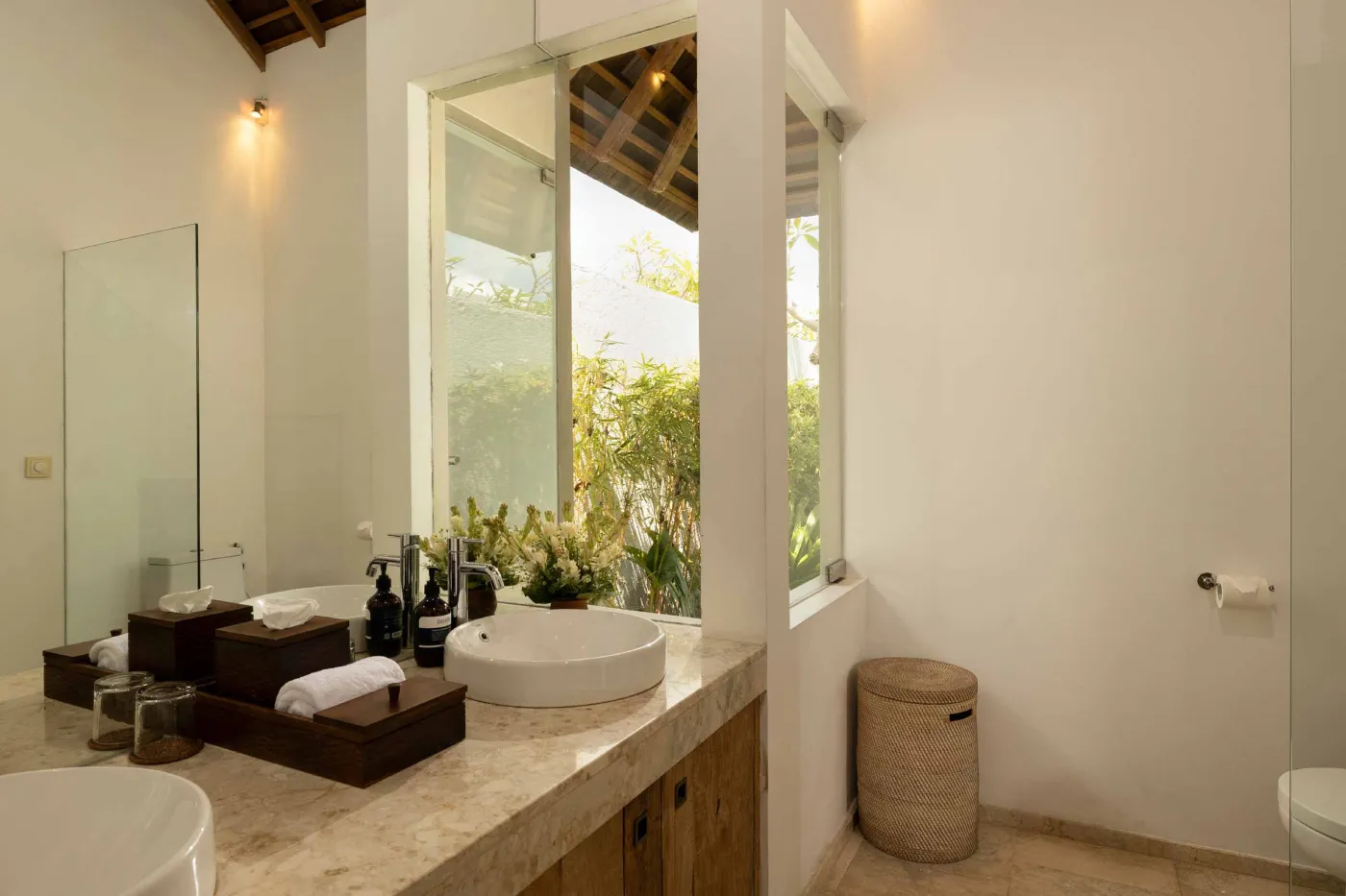 Spacious open-plan living and dining area in a modern tropical villa with exposed wooden beams, white walls, hardwood floors, and large windows. - Bali Villas