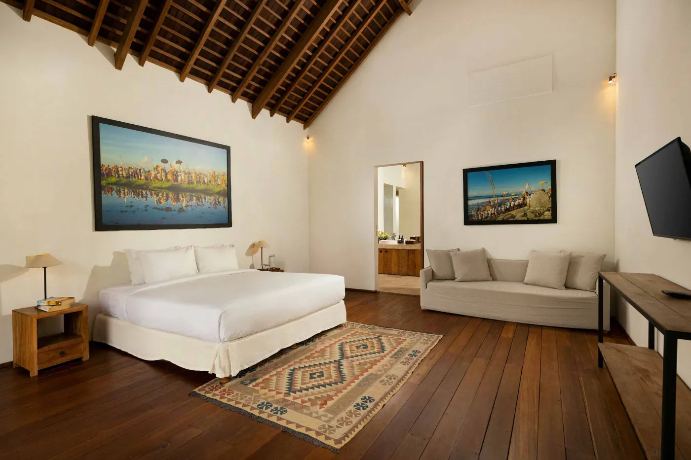 Spacious open-plan living and dining area in a modern tropical villa with exposed wooden beams, white walls, hardwood floors, and large windows. - Bali Villas