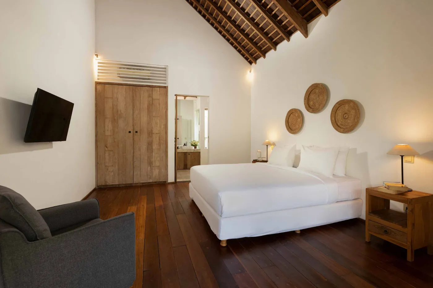 Spacious open-plan living and dining area in a modern tropical villa with exposed wooden beams, white walls, hardwood floors, and large windows. - Bali Villas