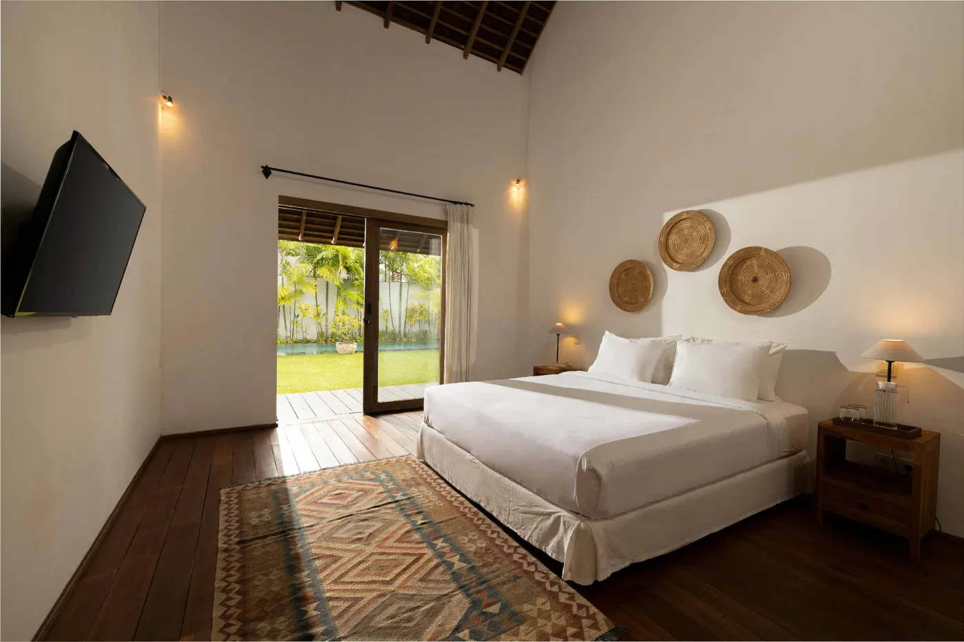 Spacious open-plan living and dining area in a modern tropical villa with exposed wooden beams, white walls, hardwood floors, and large windows. - Bali Villas