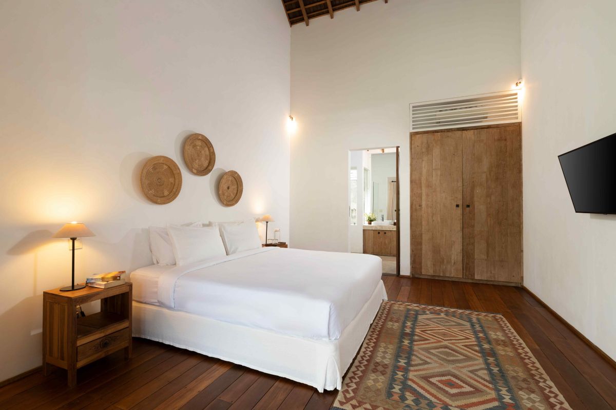 Spacious open-plan living and dining area in a modern tropical villa with exposed wooden beams, white walls, hardwood floors, and large windows. - Bali Villas