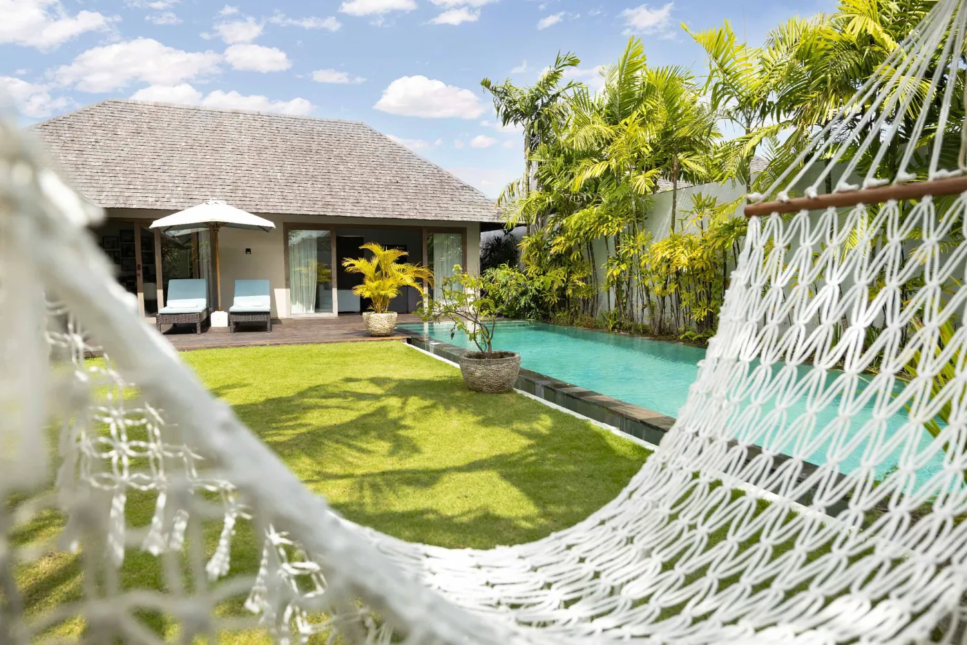 Spacious open-plan living and dining area in a modern tropical villa with exposed wooden beams, white walls, hardwood floors, and large windows. - Bali Villas