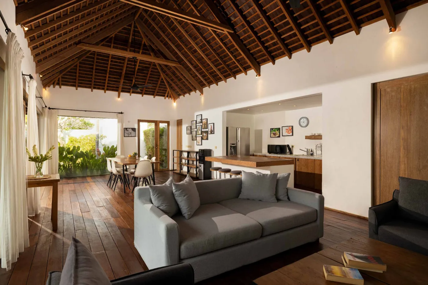 Spacious open-plan living and dining area in a modern tropical villa with exposed wooden beams, white walls, hardwood floors, and large windows. - Bali Villas