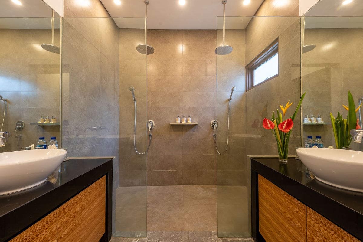 Modern luxury bathroom with freestanding bathtub filled with petals, double vessel sink vanity, glass shower, and tropical accents. - Bali Villas