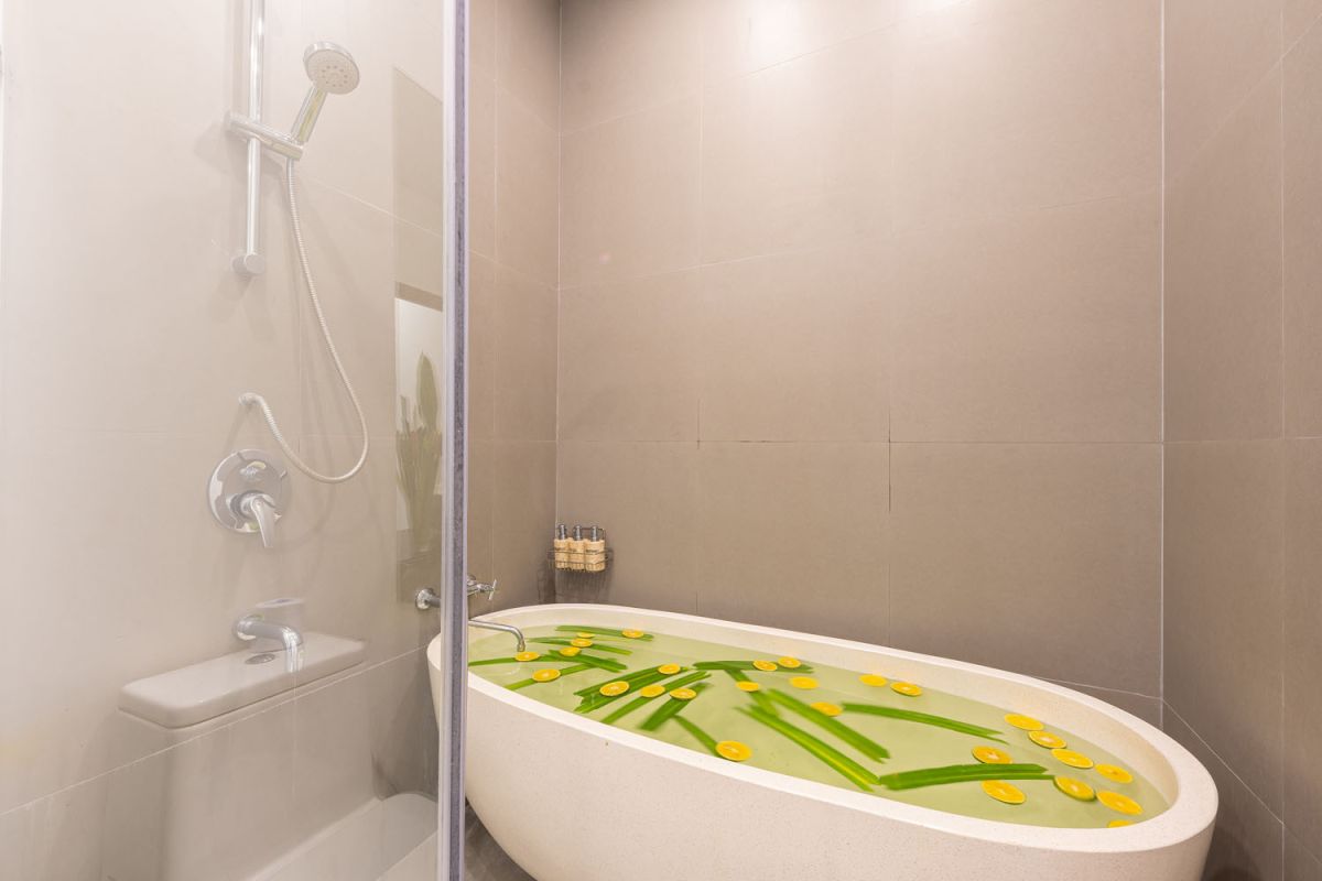 Modern luxury bathroom with freestanding bathtub filled with petals, double vessel sink vanity, glass shower, and tropical accents. - Bali Villas