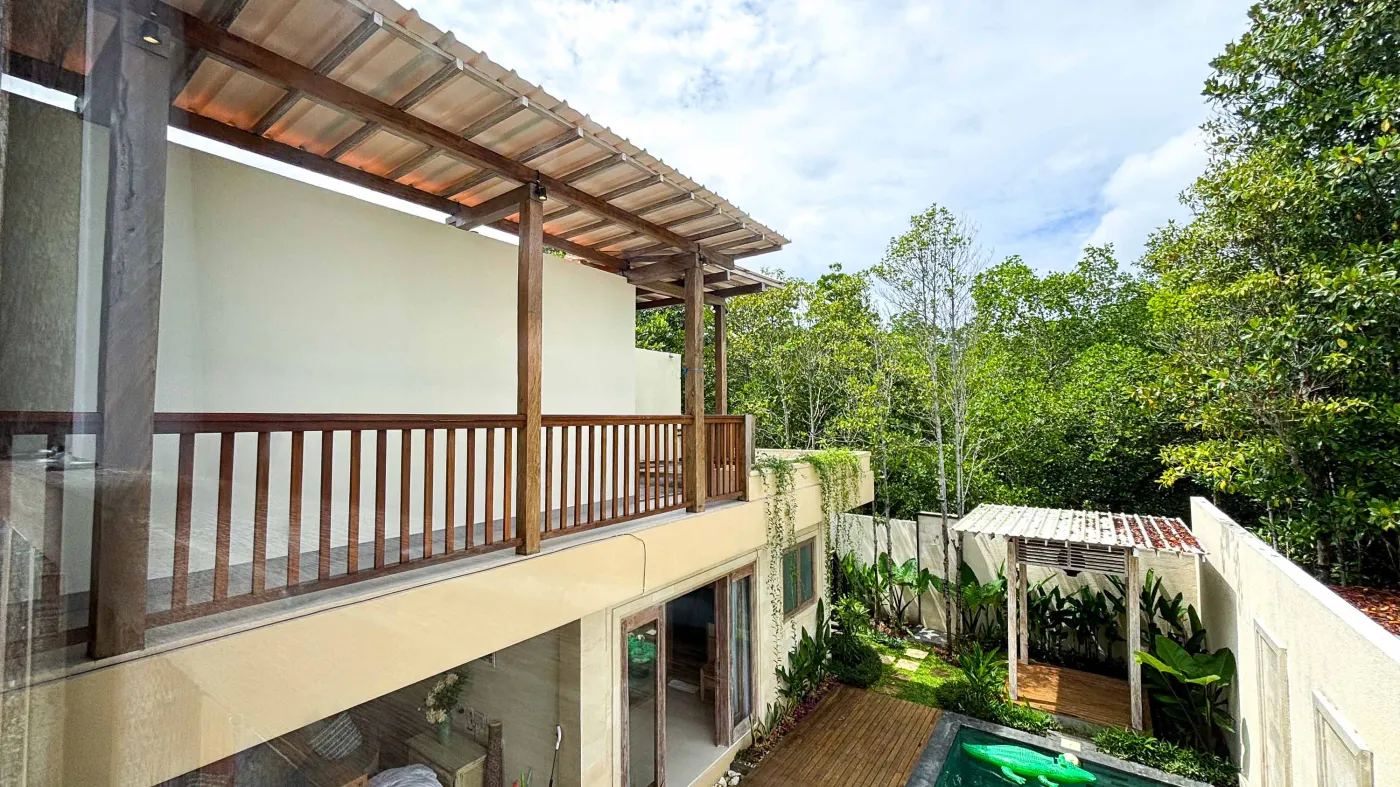 Modern bathroom with gray tile walls, corner soaking tub, wooden vanity sink, towel ladder, and rustic reclaimed wood door. - Bali Villas