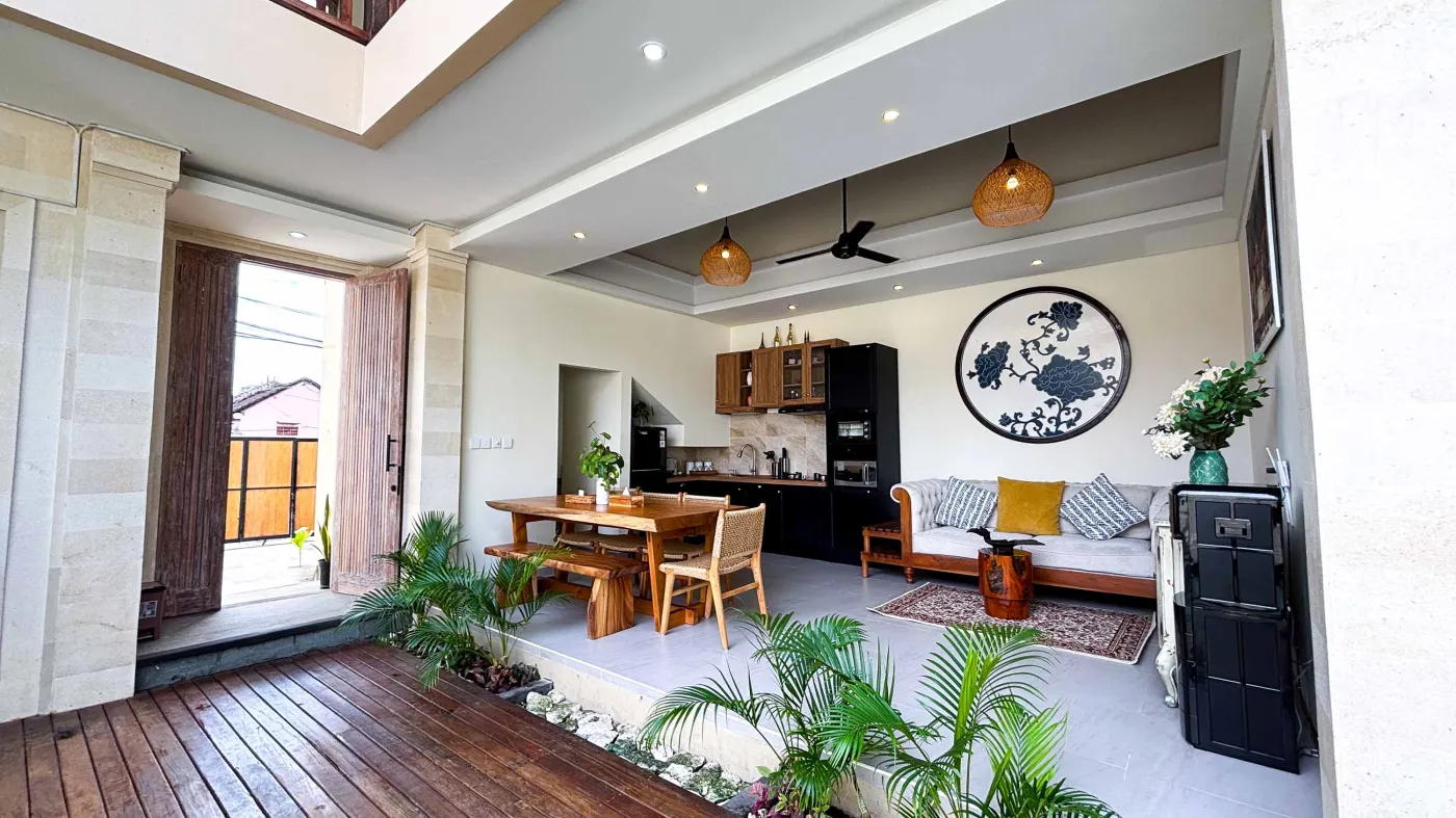 Modern bathroom with gray tile walls, corner soaking tub, wooden vanity sink, towel ladder, and rustic reclaimed wood door. - Bali Villas