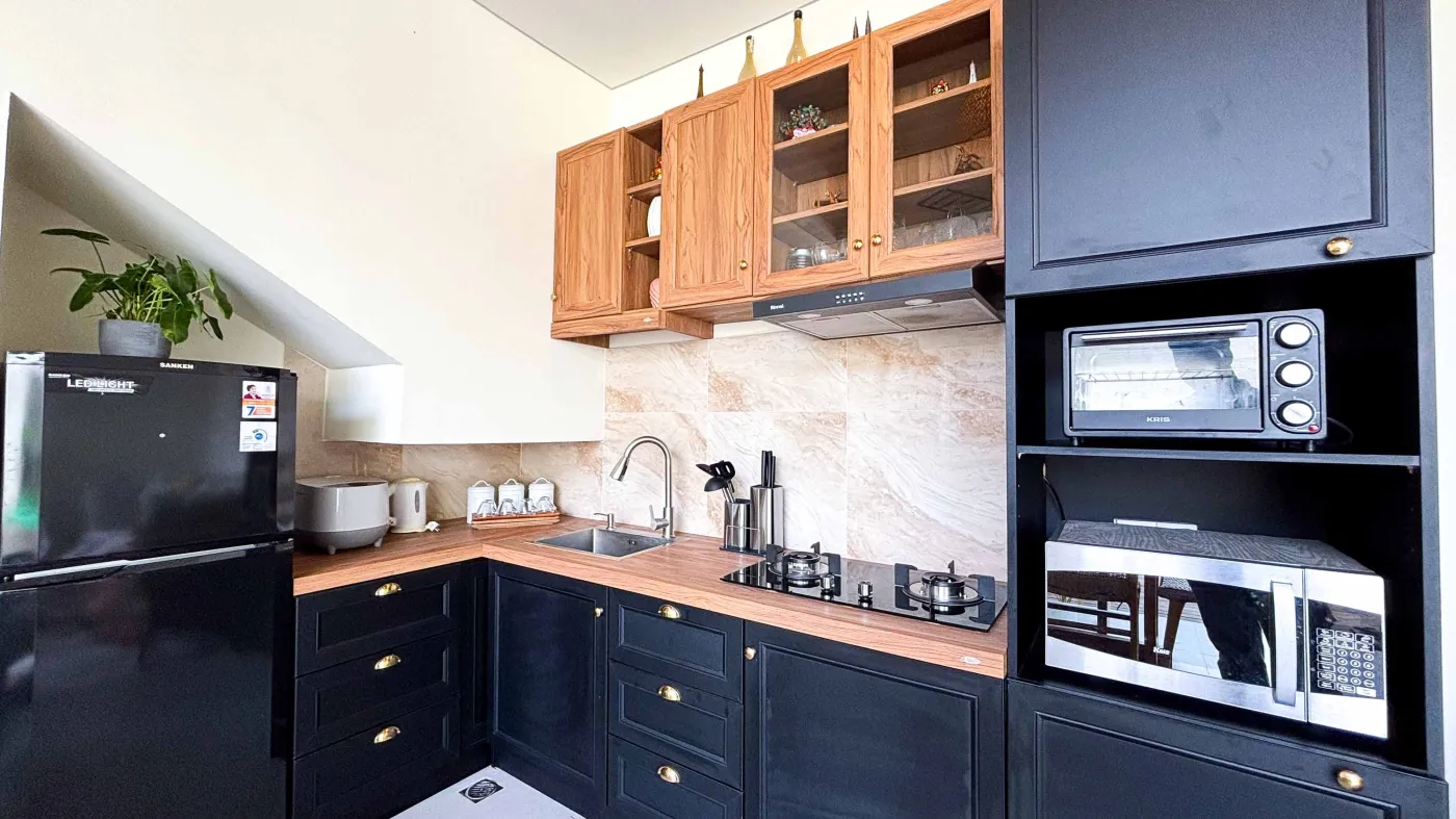 Modern bathroom with gray tile walls, corner soaking tub, wooden vanity sink, towel ladder, and rustic reclaimed wood door. - Bali Villas