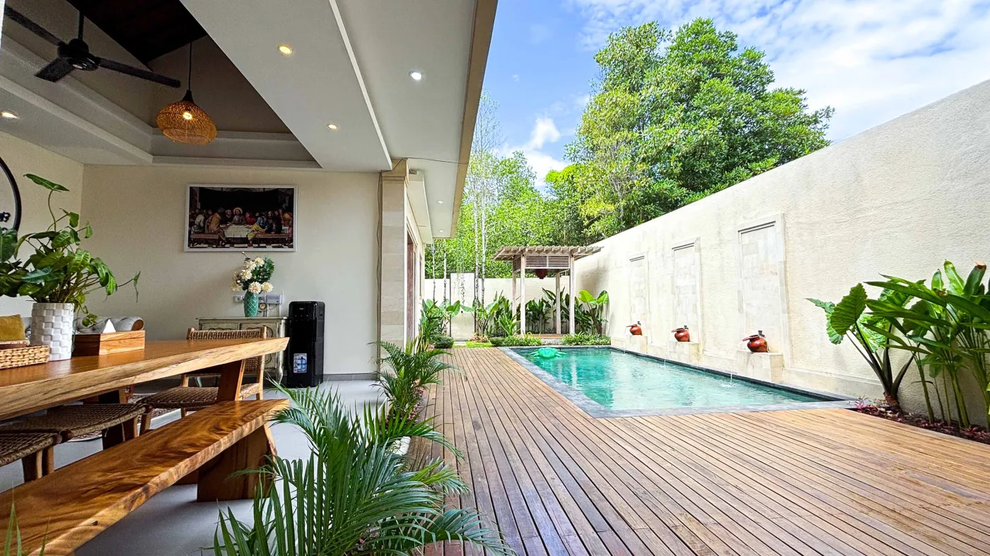 Modern bathroom with gray tile walls, corner soaking tub, wooden vanity sink, towel ladder, and rustic reclaimed wood door. - Bali Villas
