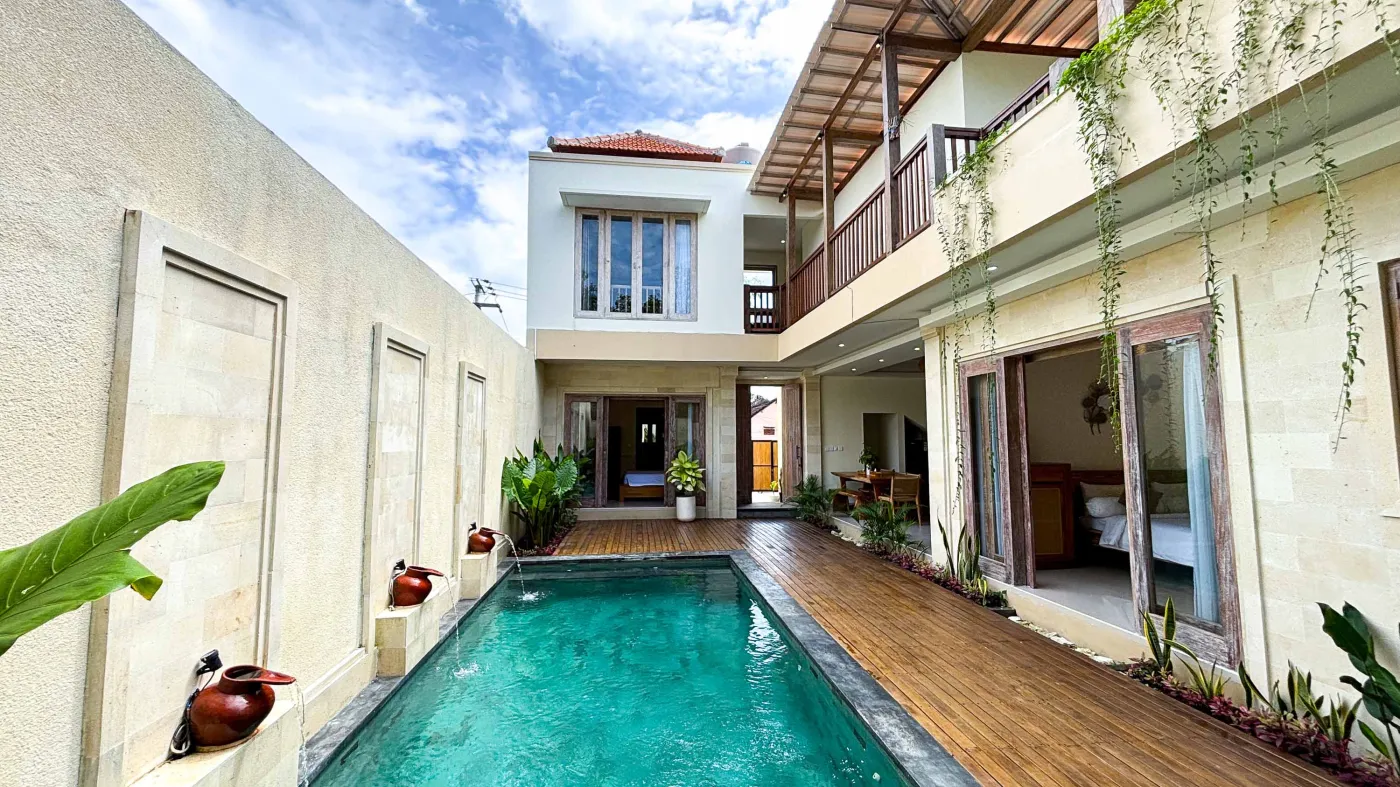 Modern bathroom with gray tile walls, corner soaking tub, wooden vanity sink, towel ladder, and rustic reclaimed wood door. - Bali Villas