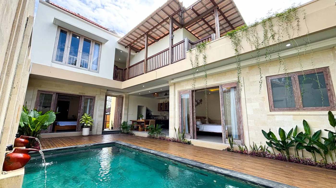 Modern bathroom with gray tile walls, corner soaking tub, wooden vanity sink, towel ladder, and rustic reclaimed wood door. - Bali Villas