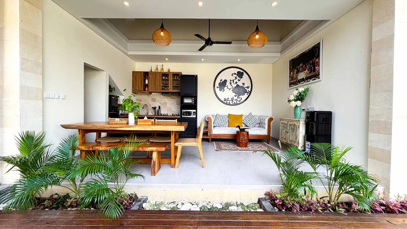 Modern bathroom with gray tile walls, corner soaking tub, wooden vanity sink, towel ladder, and rustic reclaimed wood door. - Bali Villas