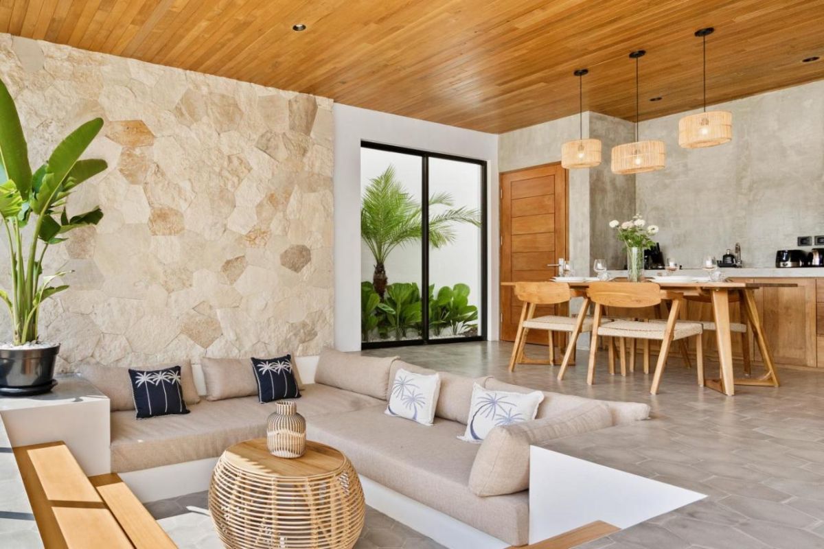 Modern tropical kitchen interior with wooden dining table, rattan pendant lights, woven wall art, and fresh flowers. - Bali Villas