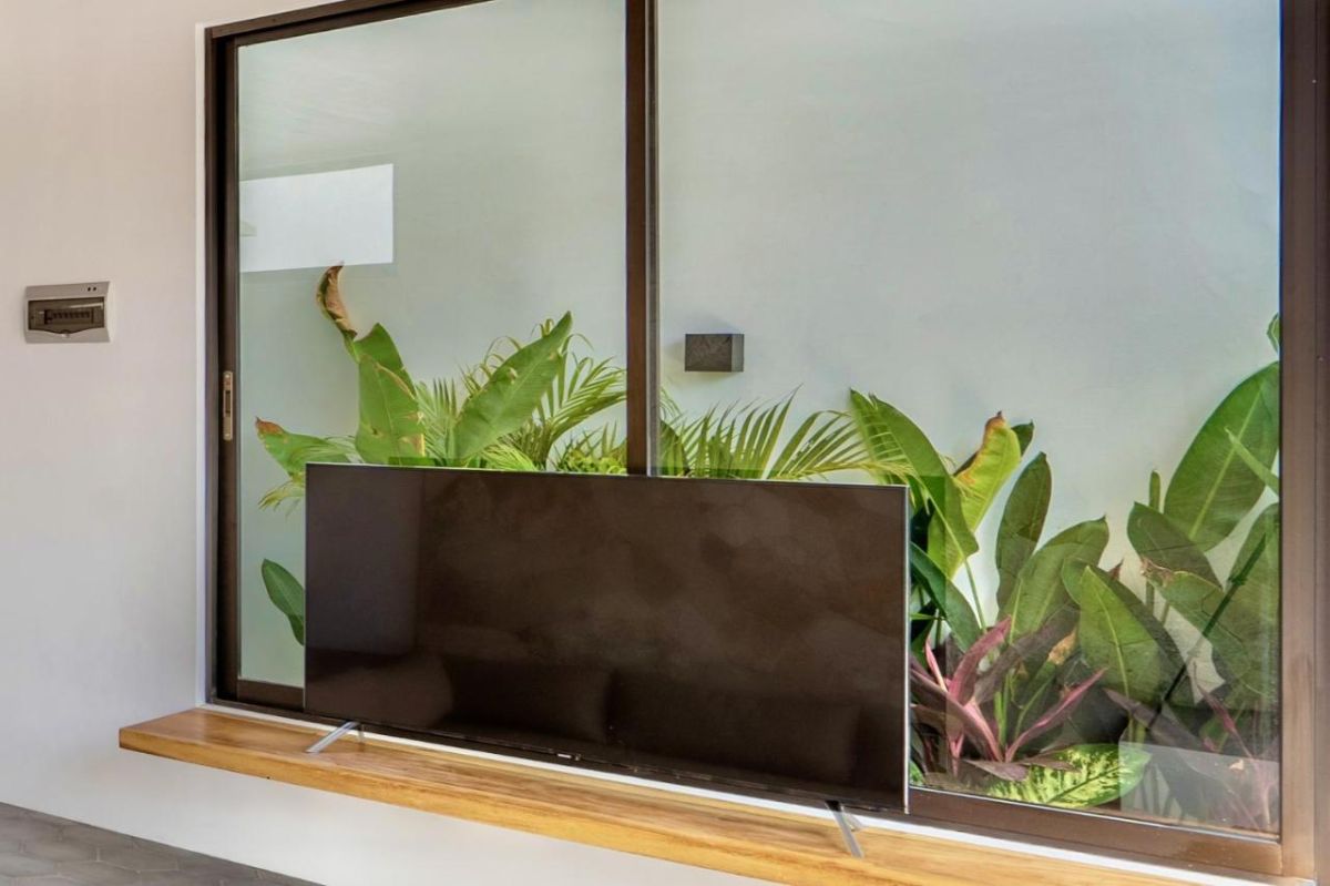 Modern tropical kitchen interior with wooden dining table, rattan pendant lights, woven wall art, and fresh flowers. - Bali Villas