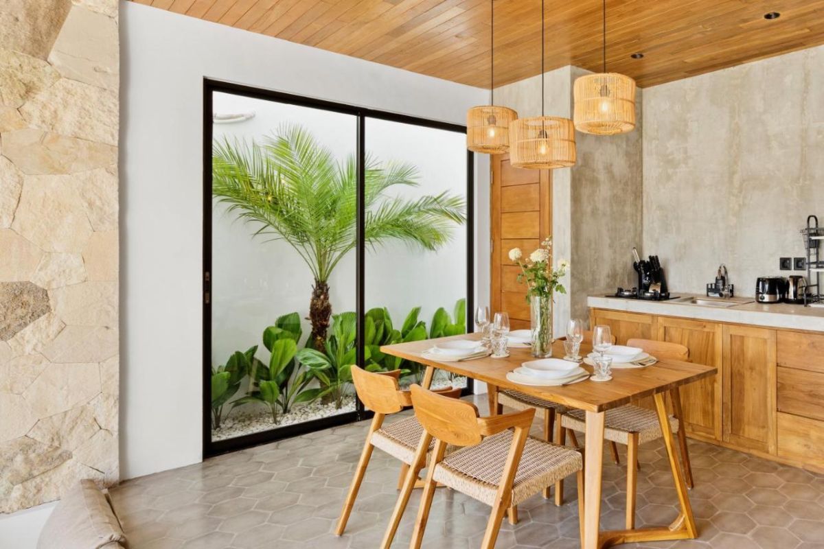Modern tropical kitchen interior with wooden dining table, rattan pendant lights, woven wall art, and fresh flowers. - Bali Villas