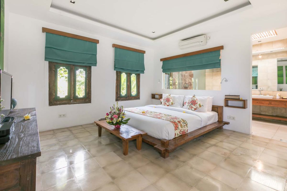 Spacious Balinese villa living room with teak wooden furniture, orange sofas, pendant lamps, and open views to tropical pool and garden. - Bali Villas