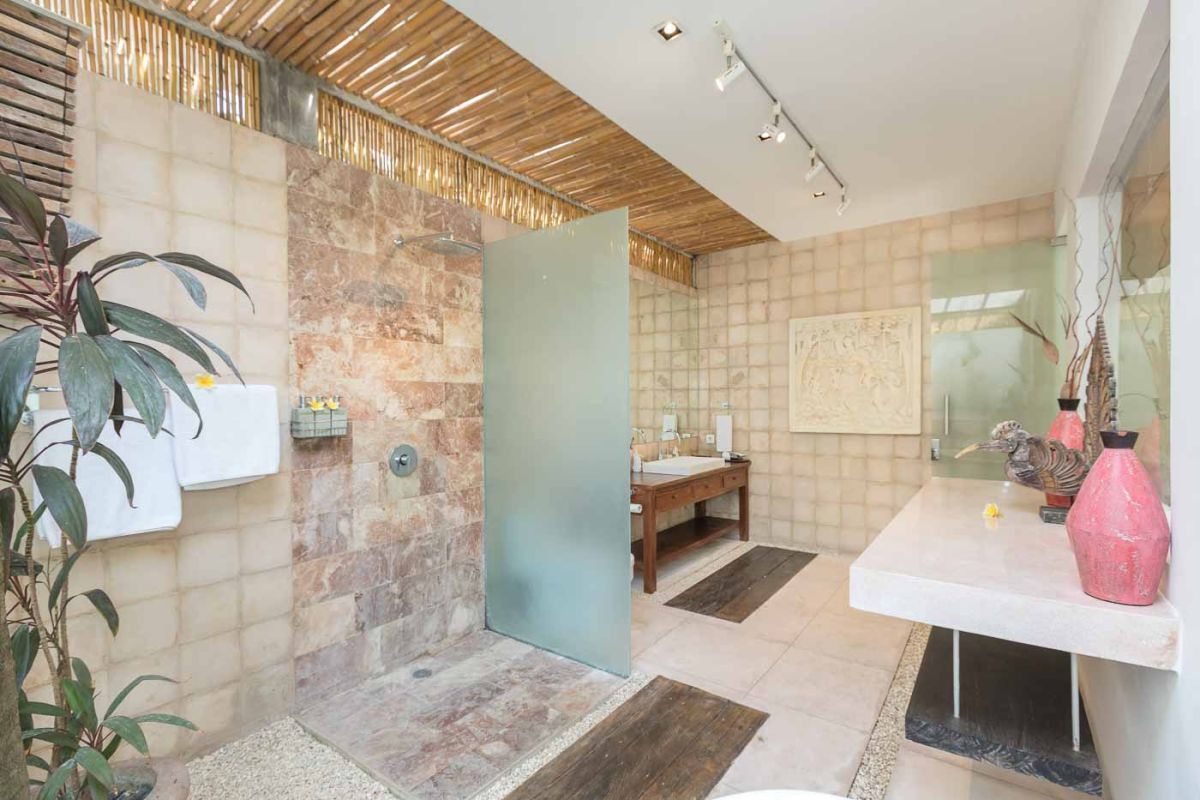 Spacious Balinese villa living room with teak wooden furniture, orange sofas, pendant lamps, and open views to tropical pool and garden. - Bali Villas