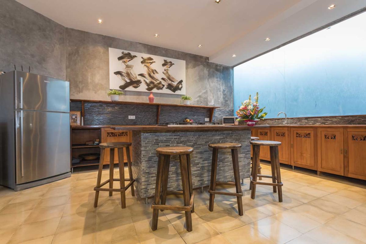 Spacious Balinese villa living room with teak wooden furniture, orange sofas, pendant lamps, and open views to tropical pool and garden. - Bali Villas