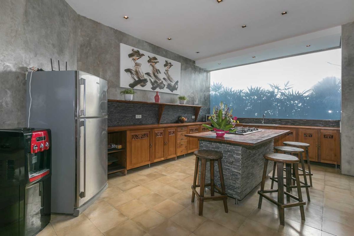 Spacious Balinese villa living room with teak wooden furniture, orange sofas, pendant lamps, and open views to tropical pool and garden. - Bali Villas