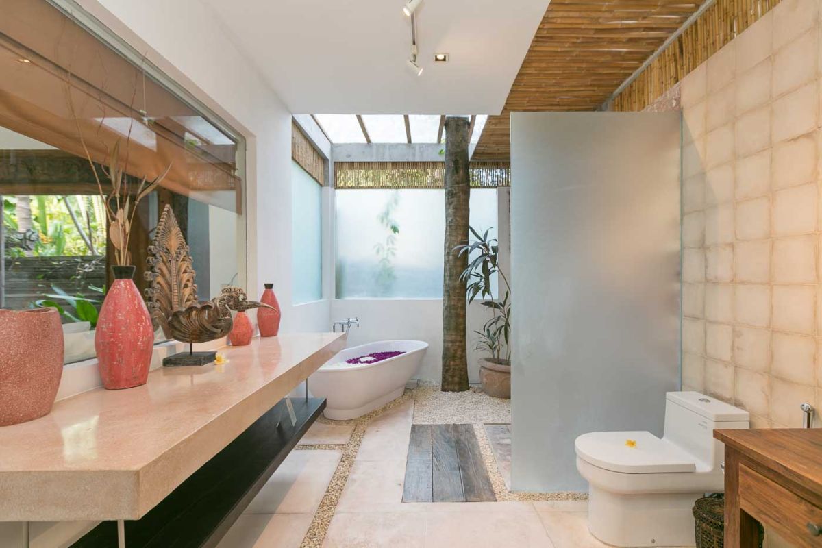 Spacious Balinese villa living room with teak wooden furniture, orange sofas, pendant lamps, and open views to tropical pool and garden. - Bali Villas