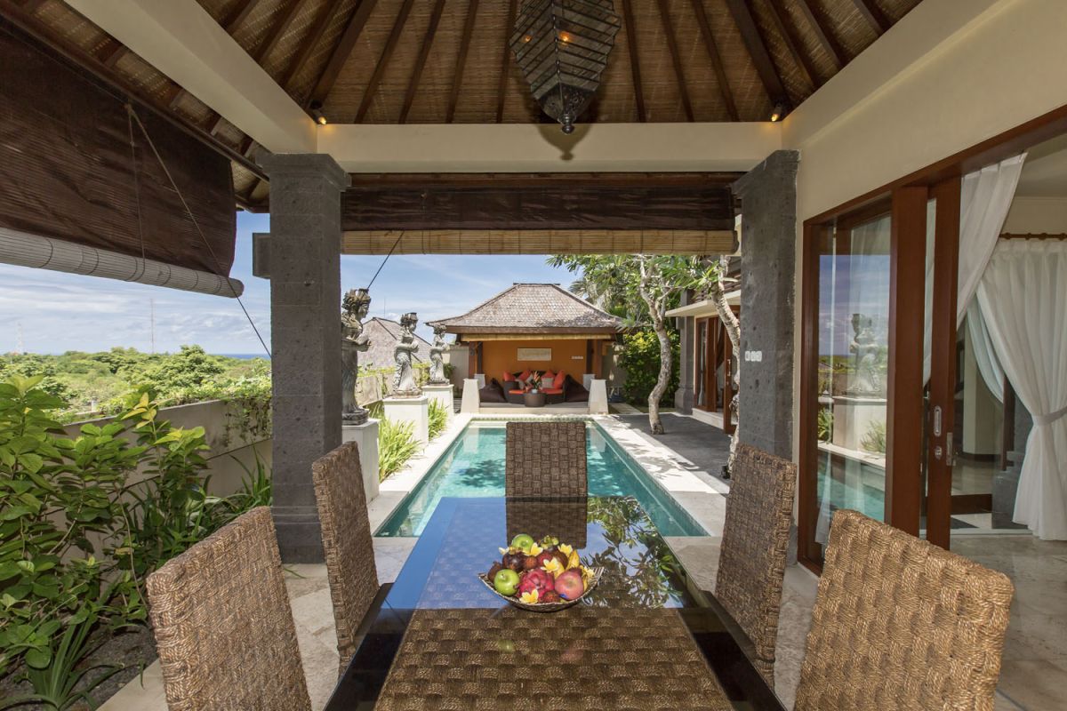 Modern luxury bathroom with beige stone tiles, freestanding white bathtub, glass shower enclosure, and wooden accents. - Bali Villas