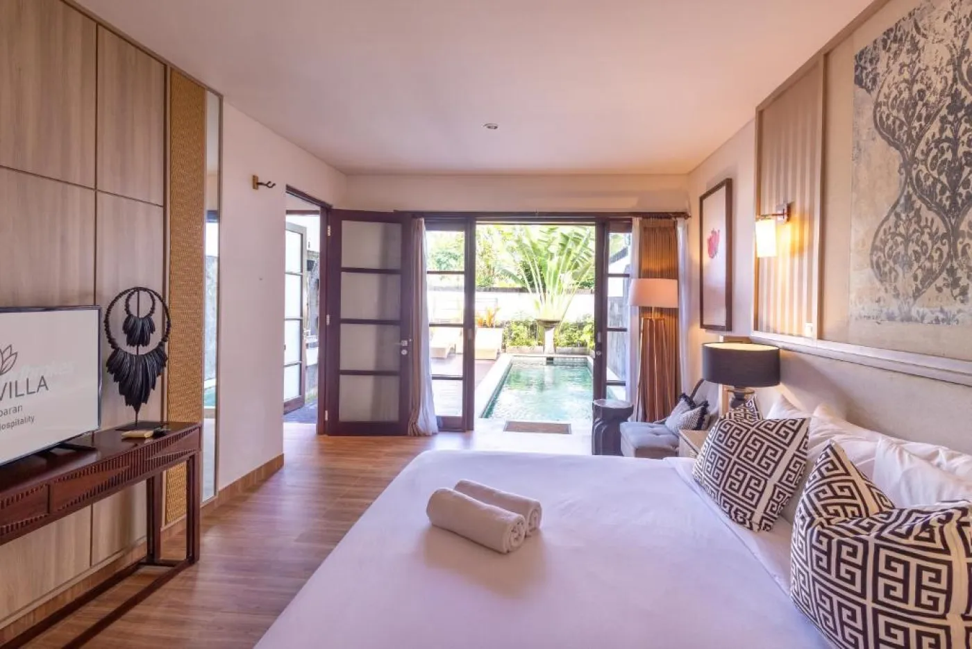Modern en-suite bathroom featuring white vanity sink, glass shower enclosure, and adjacent mirrored wardrobe on beige tiled floor. - Bali Villas