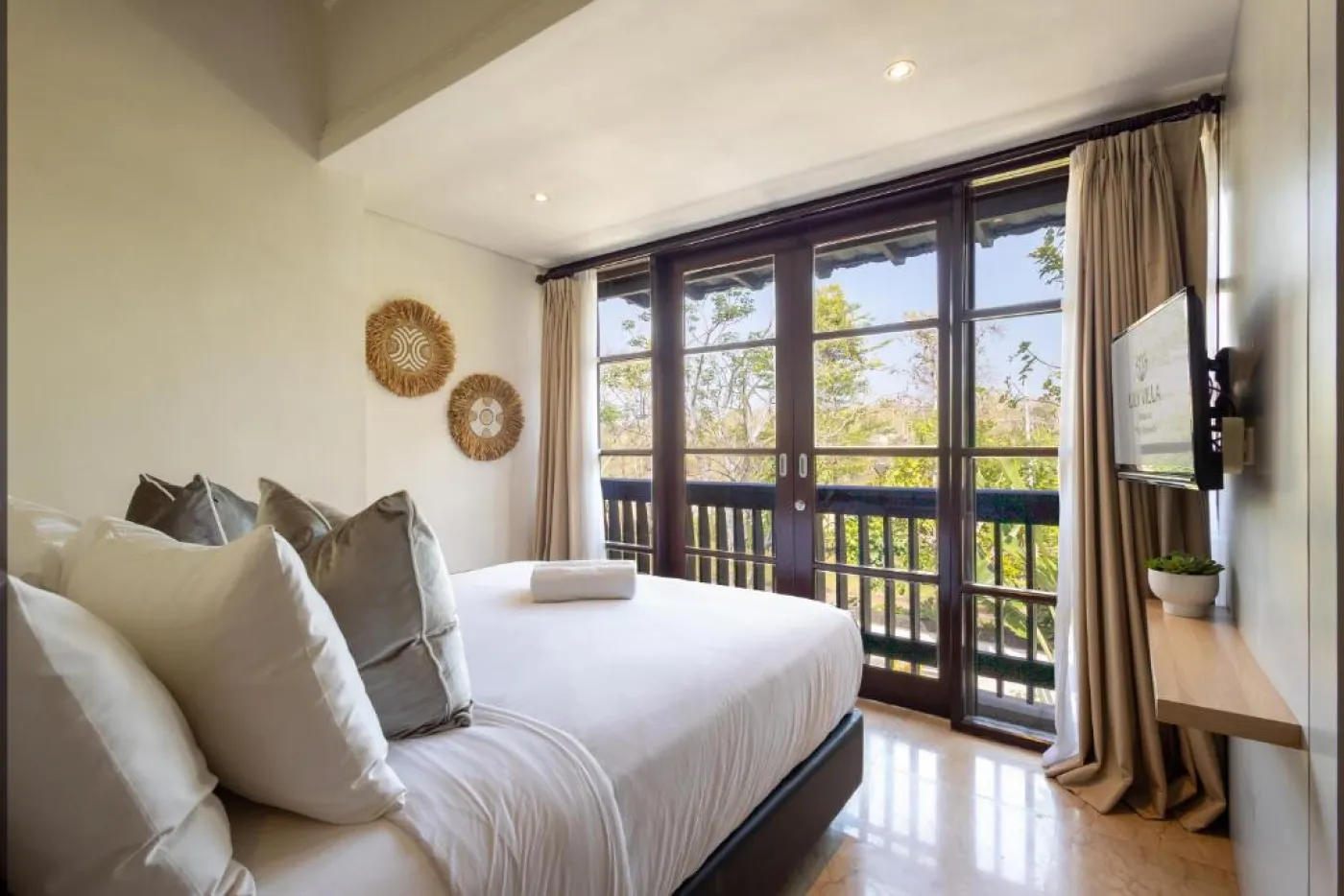 Modern en-suite bathroom featuring white vanity sink, glass shower enclosure, and adjacent mirrored wardrobe on beige tiled floor. - Bali Villas