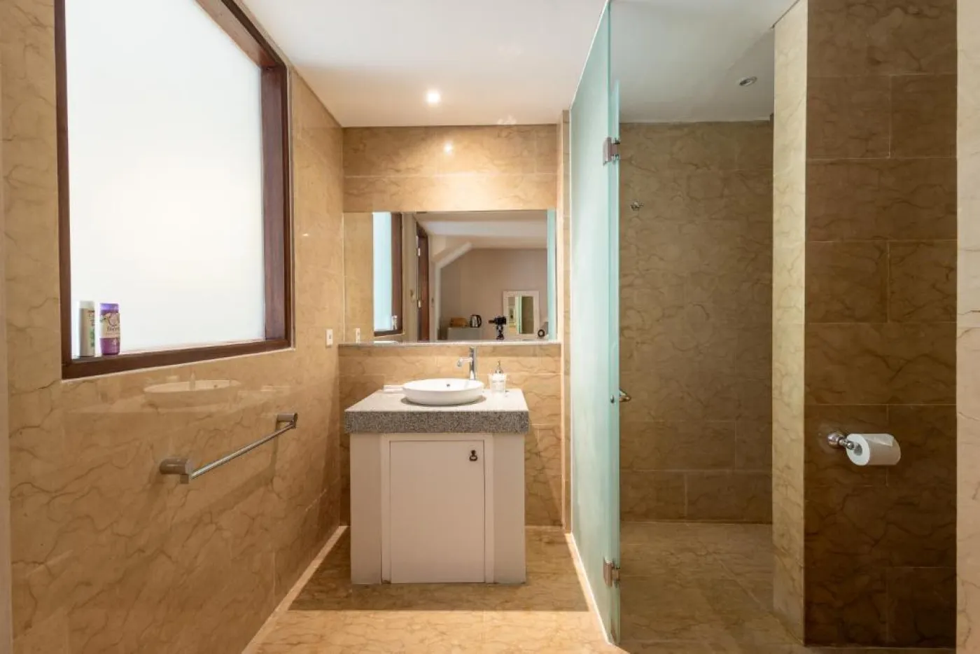 Modern en-suite bathroom featuring white vanity sink, glass shower enclosure, and adjacent mirrored wardrobe on beige tiled floor. - Bali Villas