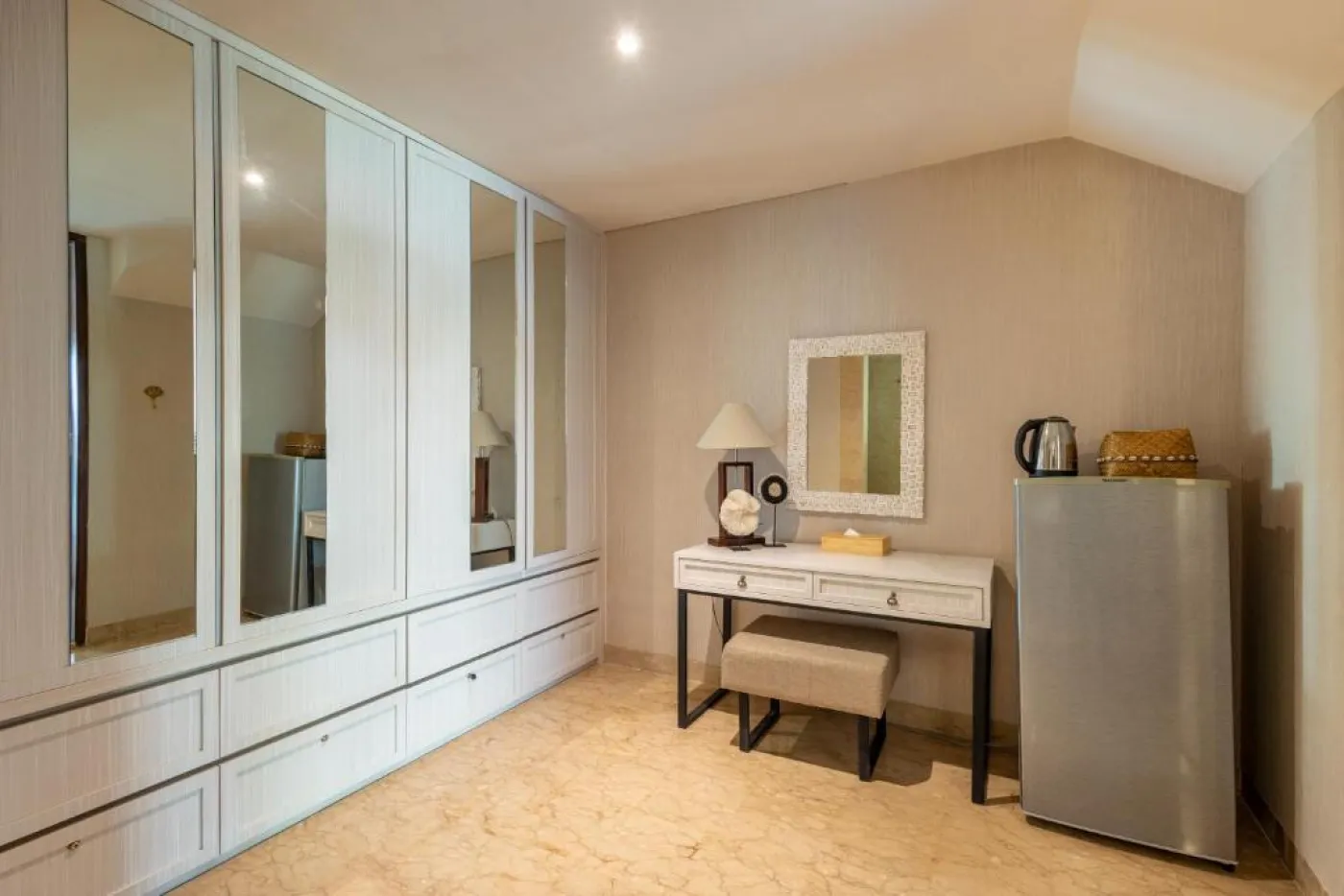 Modern en-suite bathroom featuring white vanity sink, glass shower enclosure, and adjacent mirrored wardrobe on beige tiled floor. - Bali Villas