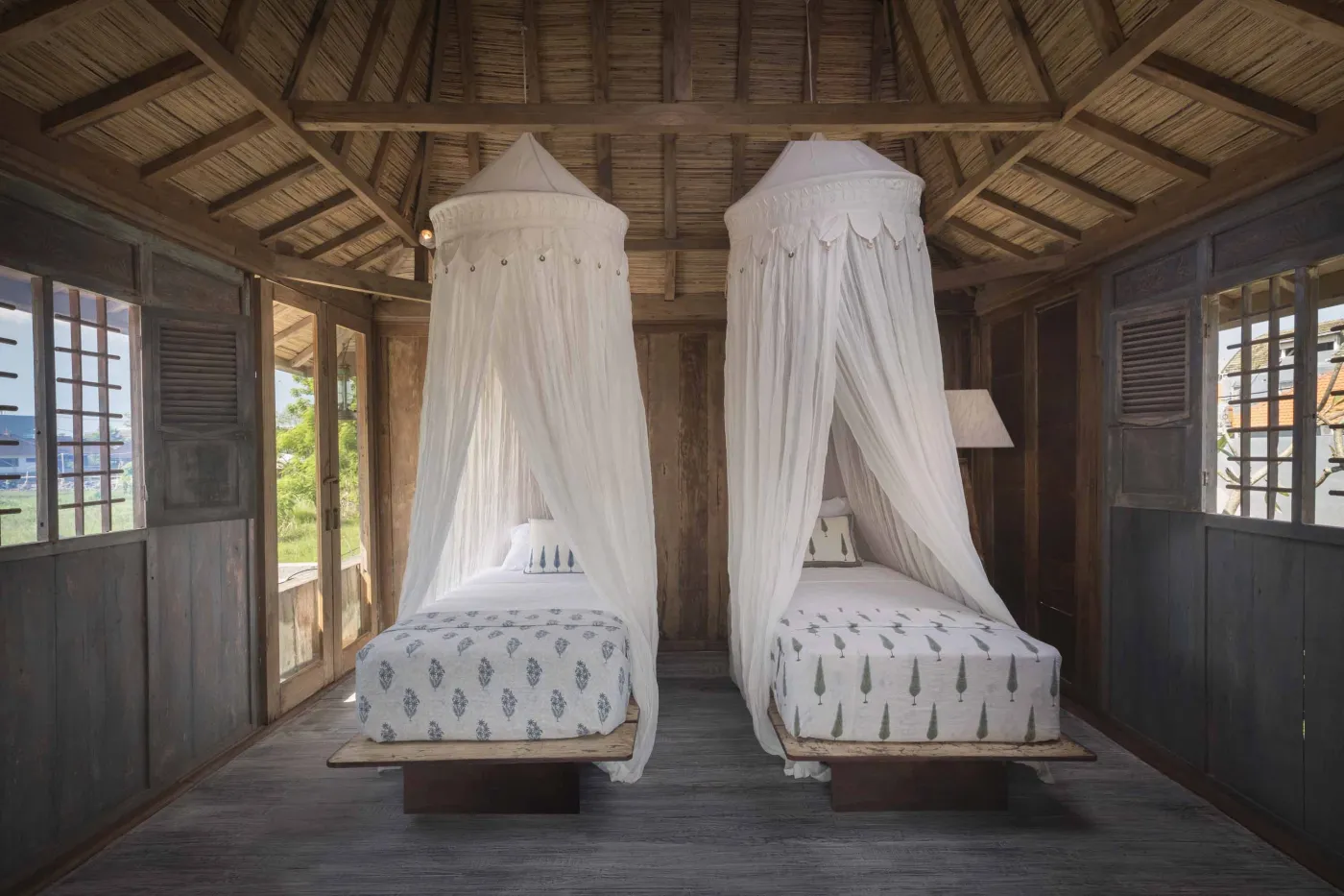 Modern Balinese villa with open-plan living room featuring white sofa, large glass doors to lush garden path, wooden accents, and red-tiled upper level. - Bali Villas