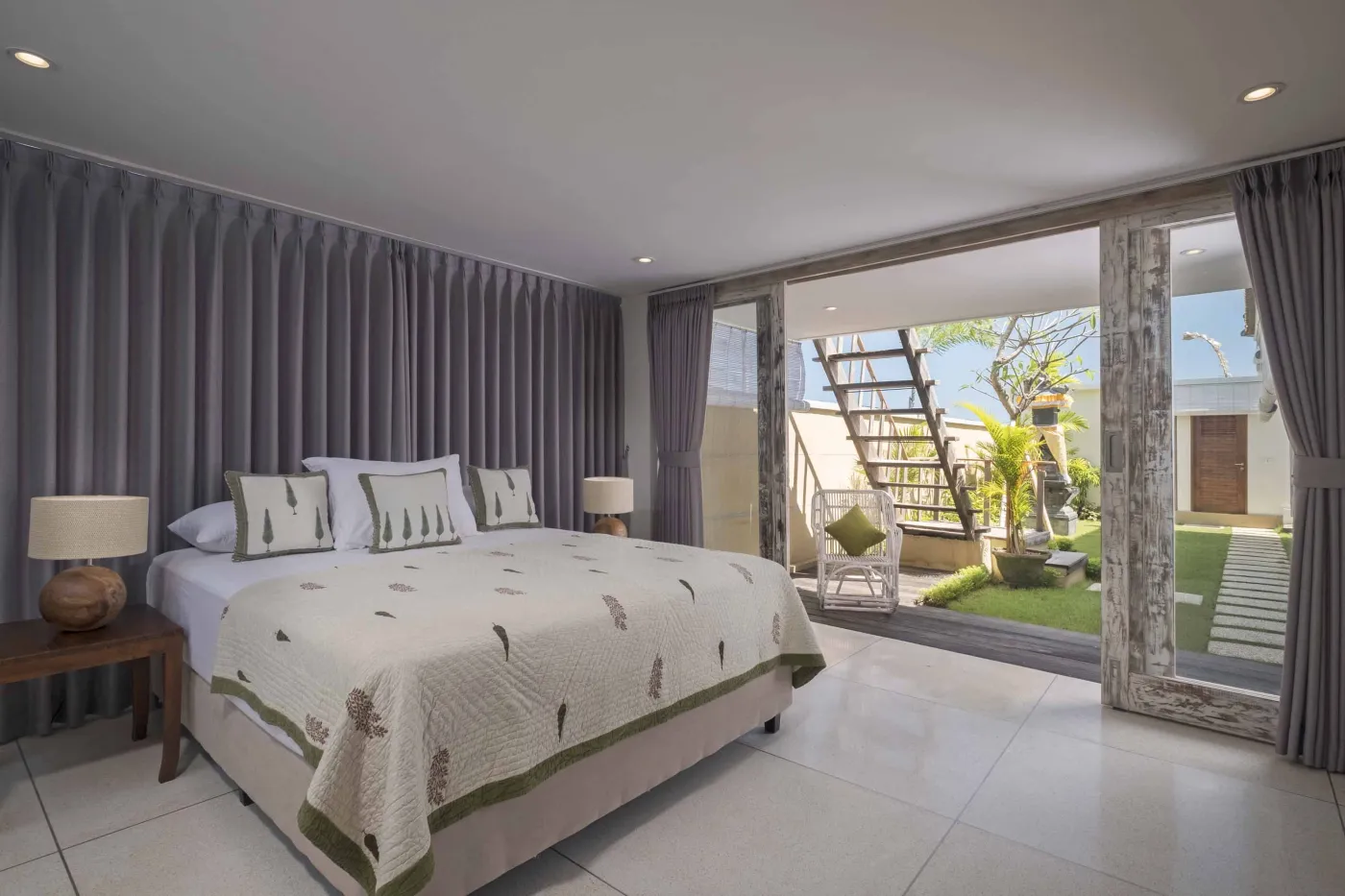 Modern Balinese villa with open-plan living room featuring white sofa, large glass doors to lush garden path, wooden accents, and red-tiled upper level. - Bali Villas