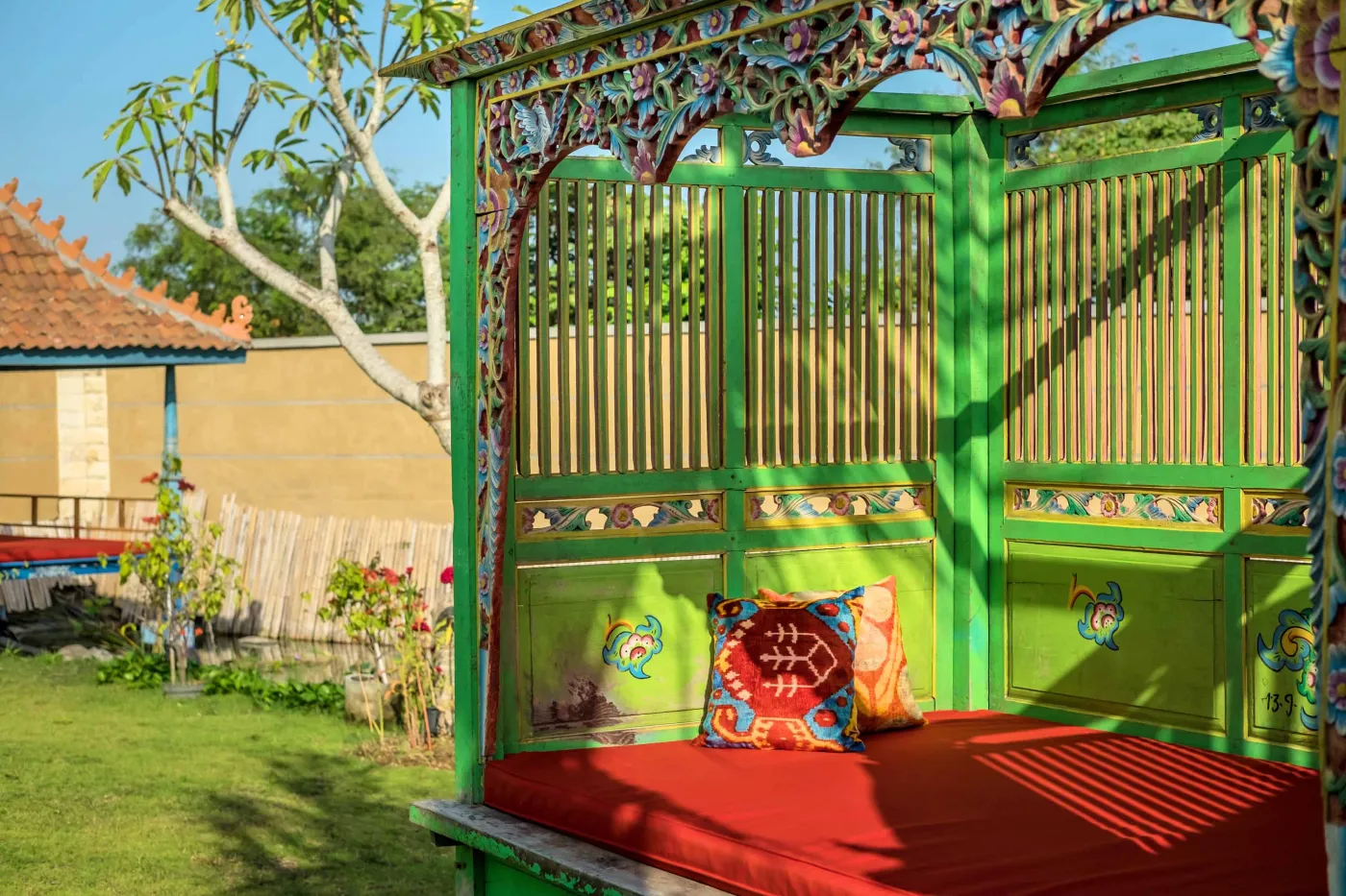 Modern Balinese villa with open-plan living room featuring white sofa, large glass doors to lush garden path, wooden accents, and red-tiled upper level. - Bali Villas