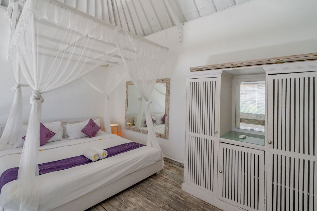 Modern minimalist living room interior with white wooden staircase, bar counter with purple stools, floral coffee table, and neutral decor. - Bali Villas
