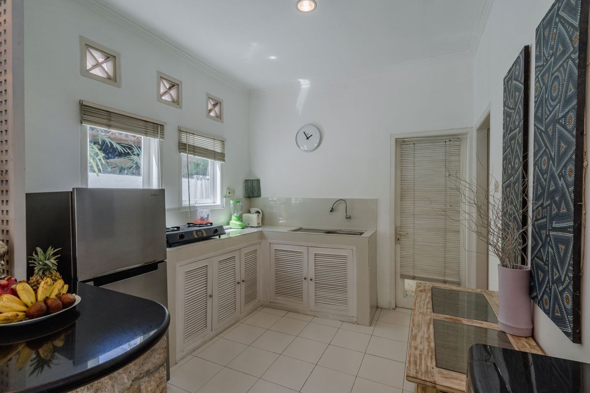 Modern minimalist living room interior with white wooden staircase, bar counter with purple stools, floral coffee table, and neutral decor. - Bali Villas