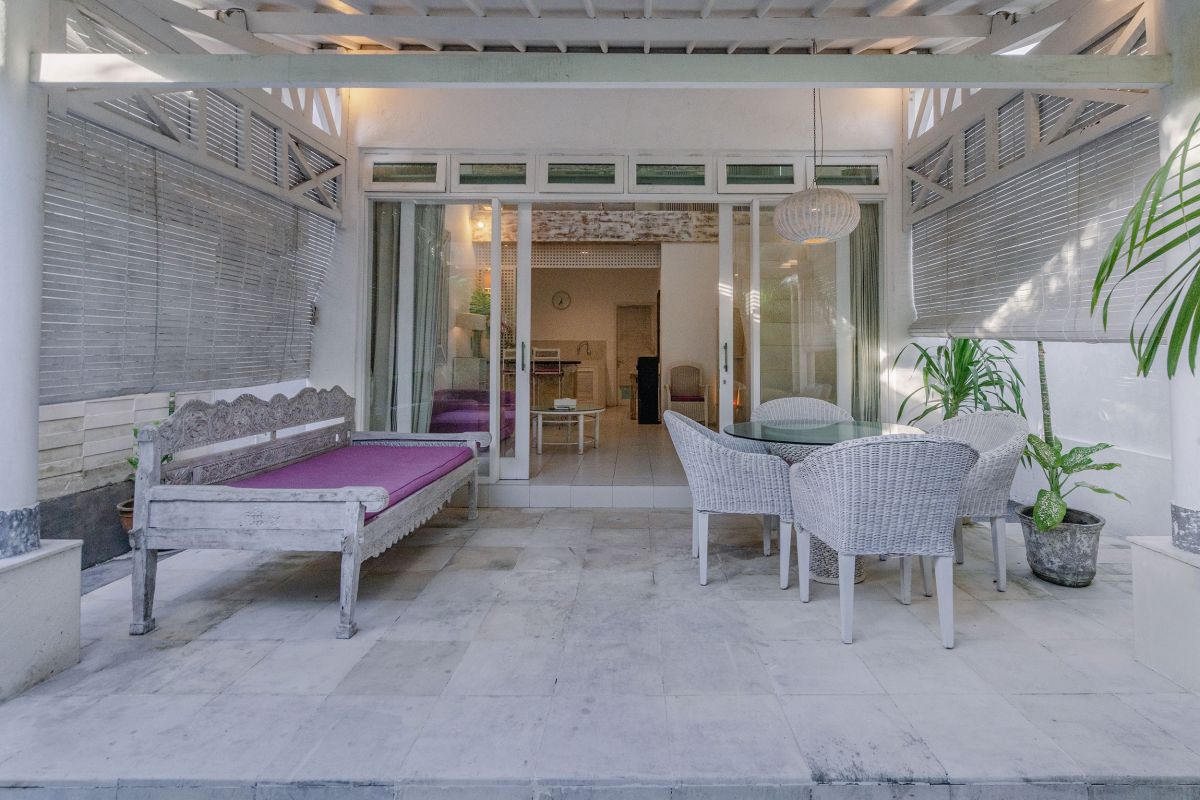 Modern minimalist living room interior with white wooden staircase, bar counter with purple stools, floral coffee table, and neutral decor. - Bali Villas